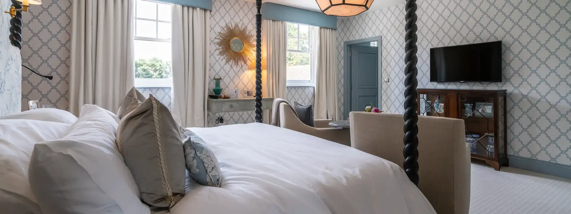 AV installation example: bedroom with a TV mounted on the patterned wall opposite a four poster bed