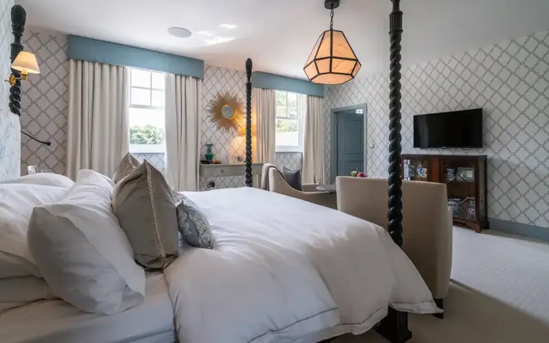 Bedroom with a TV mounted on the patterned wall opposite a four poster bed