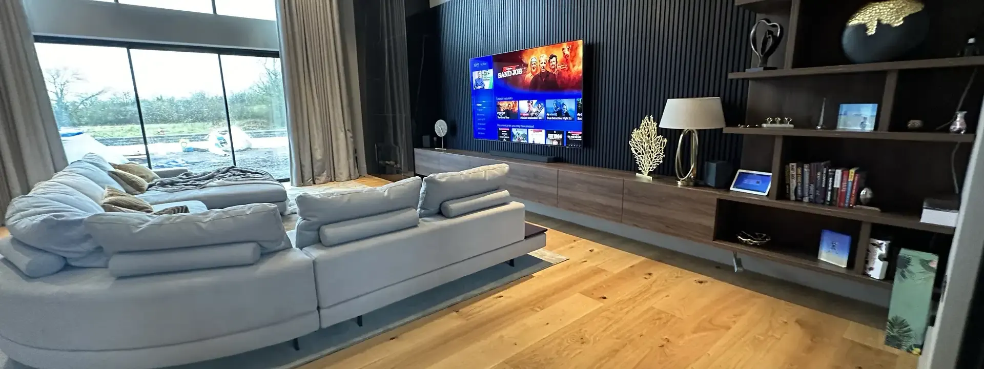 AV installers: TV mounted above a long media unit in an open family room with a corner sofa and oak floor