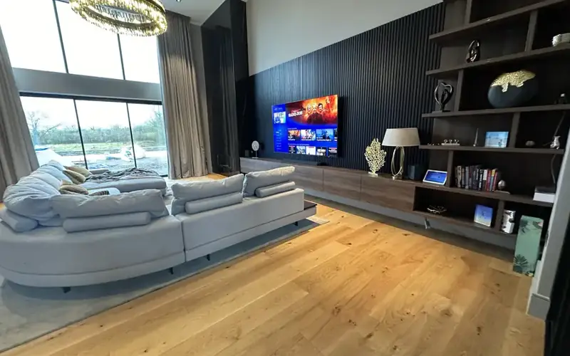 TV mounted above a long media unit in an open family room with a corner sofa and oak floor