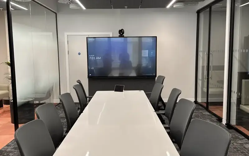 Glass walled meeting room with a video call screen and camera at the end of the table