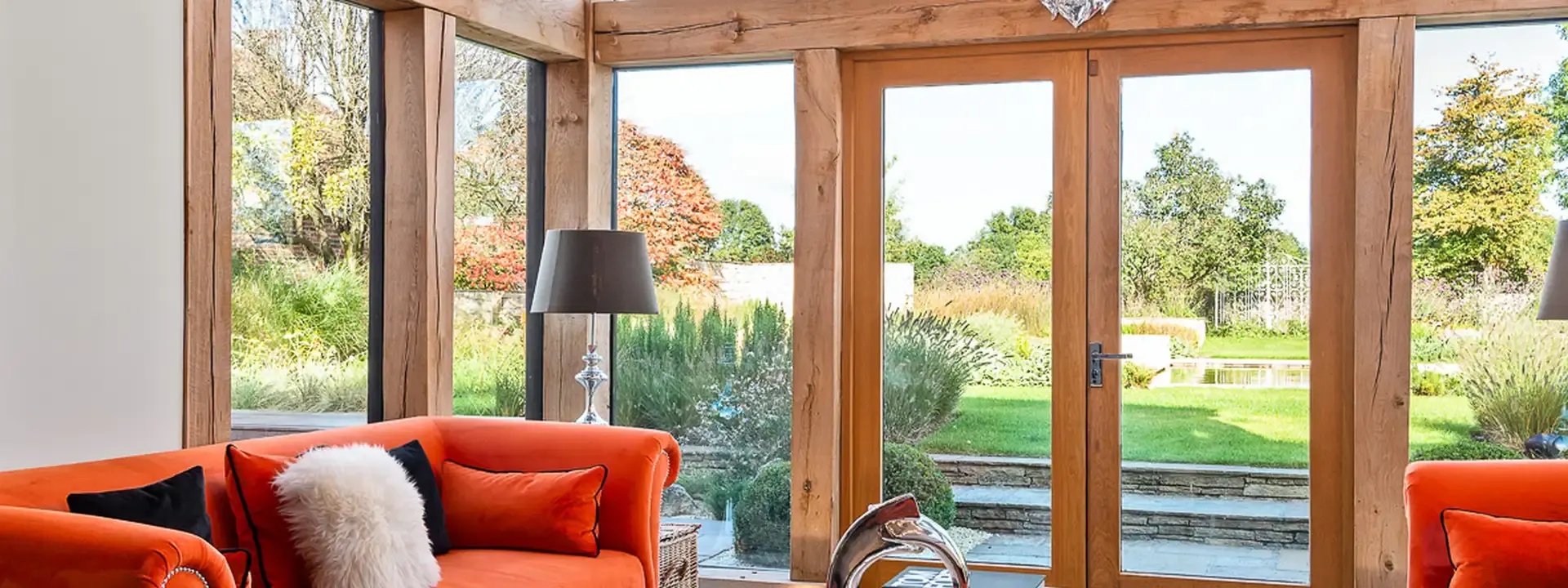 Oak framed garden room with orange sofas, glass doors and pendant bulbs