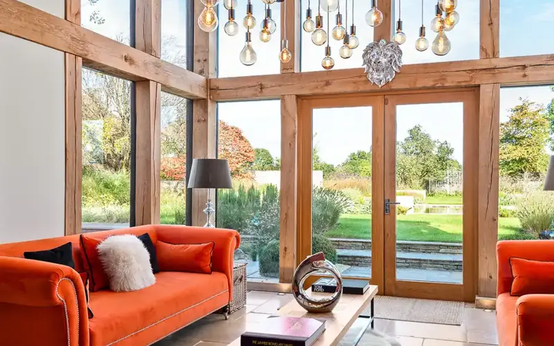 Oak framed garden room with orange sofas, glass doors and pendant bulbs